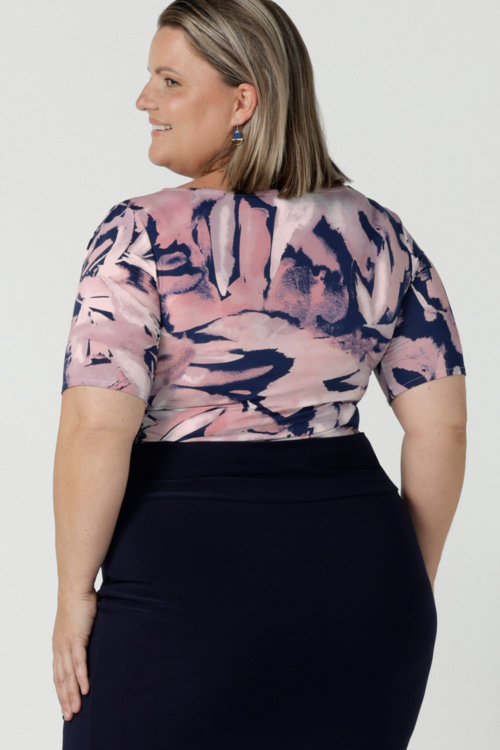 Back view of a curvy woman wears the Ziggy top in a size 18 with a boat neckline, elbow length sleeves and an abstract print on a Navy base. With painterly brush strokes. Styled back with the Andi tube skirt in Navy. Size 8 - 24
