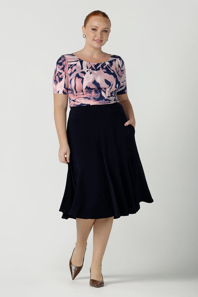 A size 12 woman wears the Ziggy top with a boat neckline, elbow length sleeves and an abstract print on a Navy base. With painterly brush strokes. Styled back with the Andi tube skirt in Navy. Inclusive sizing for women Size 8 - 24