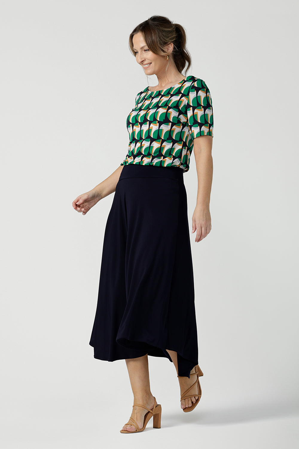  a size 10 woman wearing a boat neck short sleeve jersey top in a geometric print. She wears the top with a navy skirt. Designed and made in Australia for petite to plus size women.