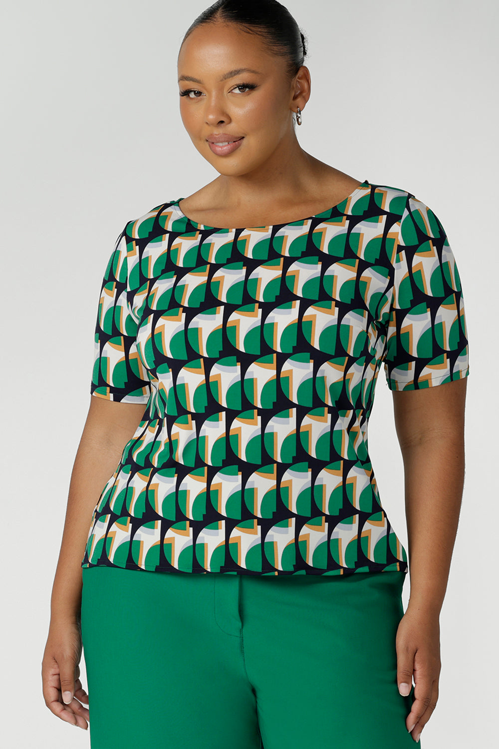 A curvy size 18 woman wears a boat neck elbow length sleeve jersey top in a geometric print. She wears the top. Designed and made in Australia for petite to plus size women.