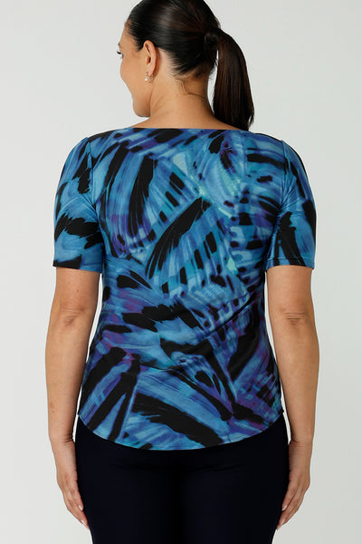Back view of a size 12 woman wearing boat neckline Ziggy top in Flutter. A cobalt and purple print on a black base that is digitally printed. Made in Australia in soft Jersey with elbow length sleeves. A great work to weekend top. Size 8 - 24. Styled back with black slim fit Brooklyn pants.