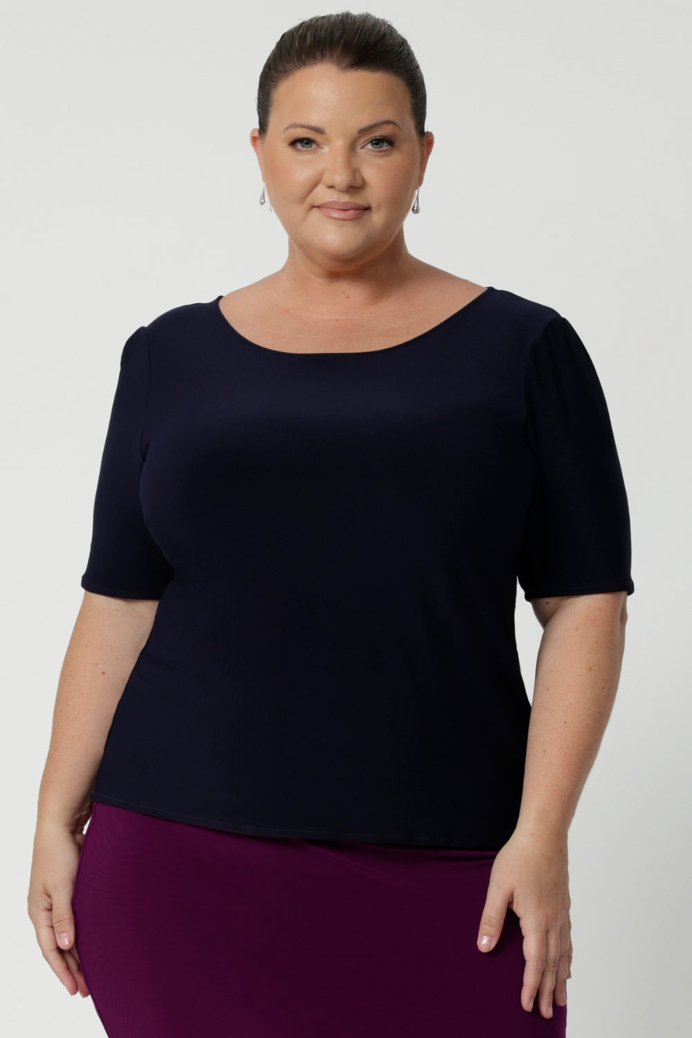 Plus size woman wears navy workwear top featuring elbow sleeves, straight neckline and straight hem. Styled with magenta coloured tube skirt and heels for an elevated look for work. Available in size 8-24.