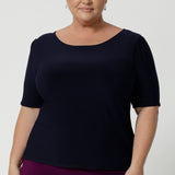 Plus size woman wears navy workwear top featuring elbow sleeves, straight neckline and straight hem. Styled with magenta coloured tube skirt and heels for an elevated look for work. Available in size 8-24.