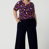 Size 18 curvy woman wears the Ziggy top in Palette. A boat neckline style with short sleeves and shoulder tucks. A great work to weekend top for women. Palette print features a brush stroke print of fuchsia, lilac, red and orange . Made in Australia for women size 8 to 24.Styled back with Bradley culottes in Navy.