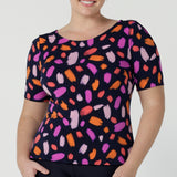 Size 12 happy woman wears the Ziggy top in Palette. A boat neckline style with short sleeves and shoulder tucks. A great work to weekend top for women. Palette print features a brush stroke print of fuchsia, lilac, red and orange . Made in Australia for women size 8 to 24.