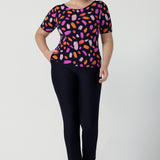 Size 12 woman wears the Ziggy top in Palette. A boat neckline style with short sleeves and shoulder tucks. A great work to weekend top for women. Palette print features a brush stroke print of fuchsia, lilac, red and orange . Made in Australia for women size 8 to 24.Styled back with Brooklyn pants in Navy. 