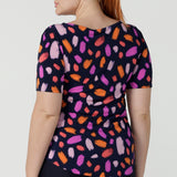 Back view of a size 12 happy woman wears the Ziggy top in Palette. A boat neckline style with short sleeves and shoulder tucks. A great work to weekend top for women. Palette print features a brush stroke print of fuchsia, lilac, red and orange . Made in Australia for women size 8 to 24.