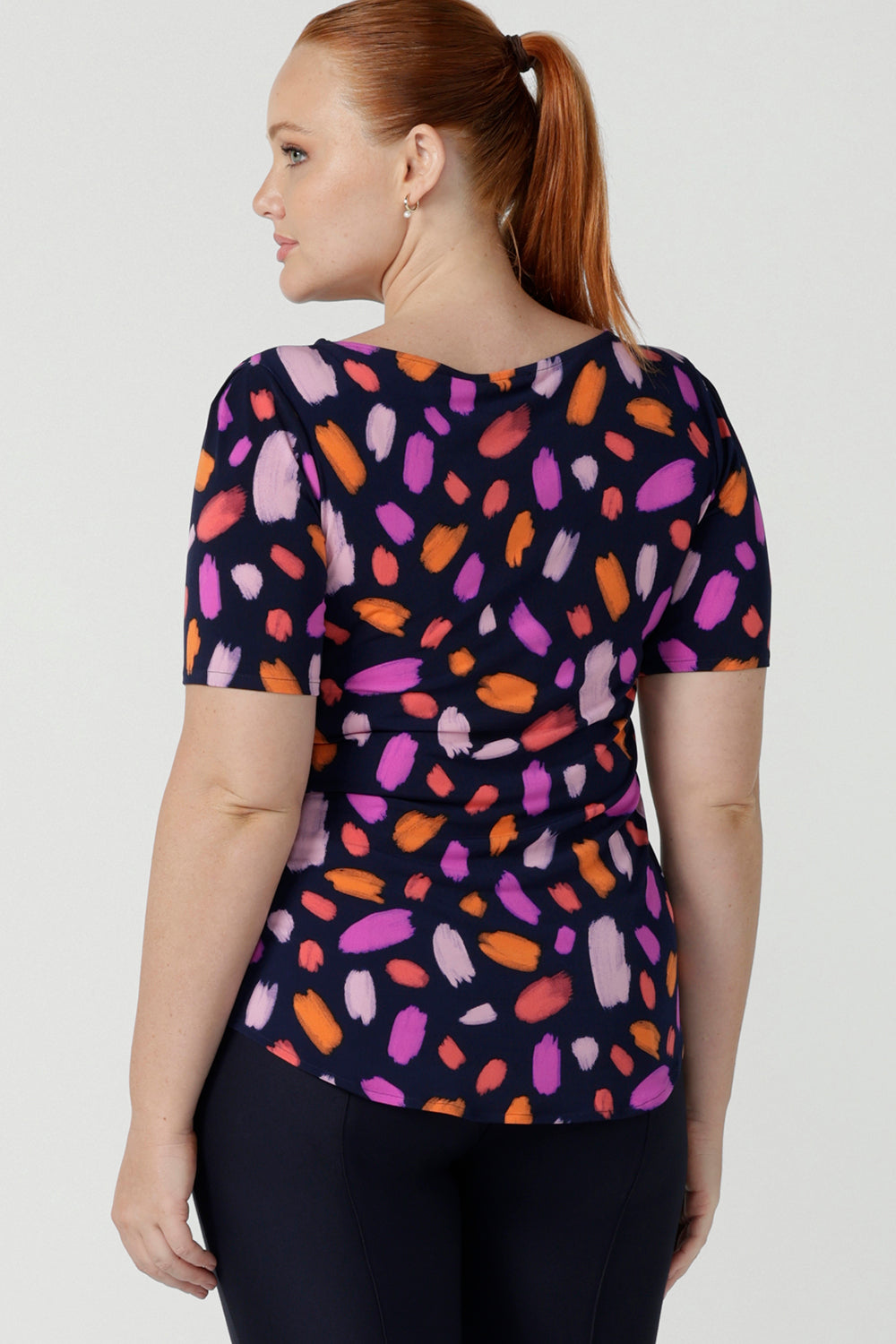 Back view of a size 12 happy woman wears the Ziggy top in Palette. A boat neckline style with short sleeves and shoulder tucks. A great work to weekend top for women. Palette print features a brush stroke print of fuchsia, lilac, red and orange . Made in Australia for women size 8 to 24.