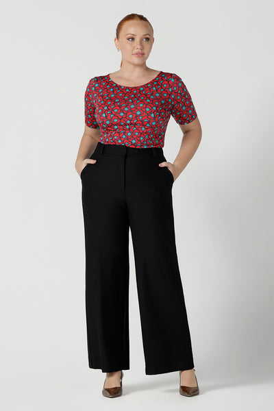 Size 12 woman wears the Ziggy top in Rio with a red base and seventies style floral. Round and conservative neckline. Short sleeve and made in Australia for women size 8 - 24. Styled back with Black Kade pants, a corporate tailored pant in black.