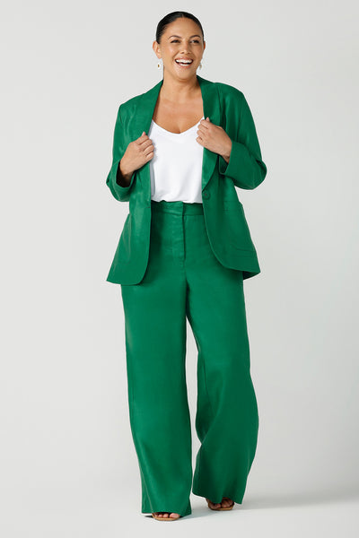 A size 12, curvy woman wears tailored linen, wide leg pants in emerald green with a longline, tailored blazer in emerald green and a white cami top in bamboo jersey. fabric - great for women's workwear! Both are made in Australia by Australian and New Zealand women's clothing brand, Leina & Fleur.