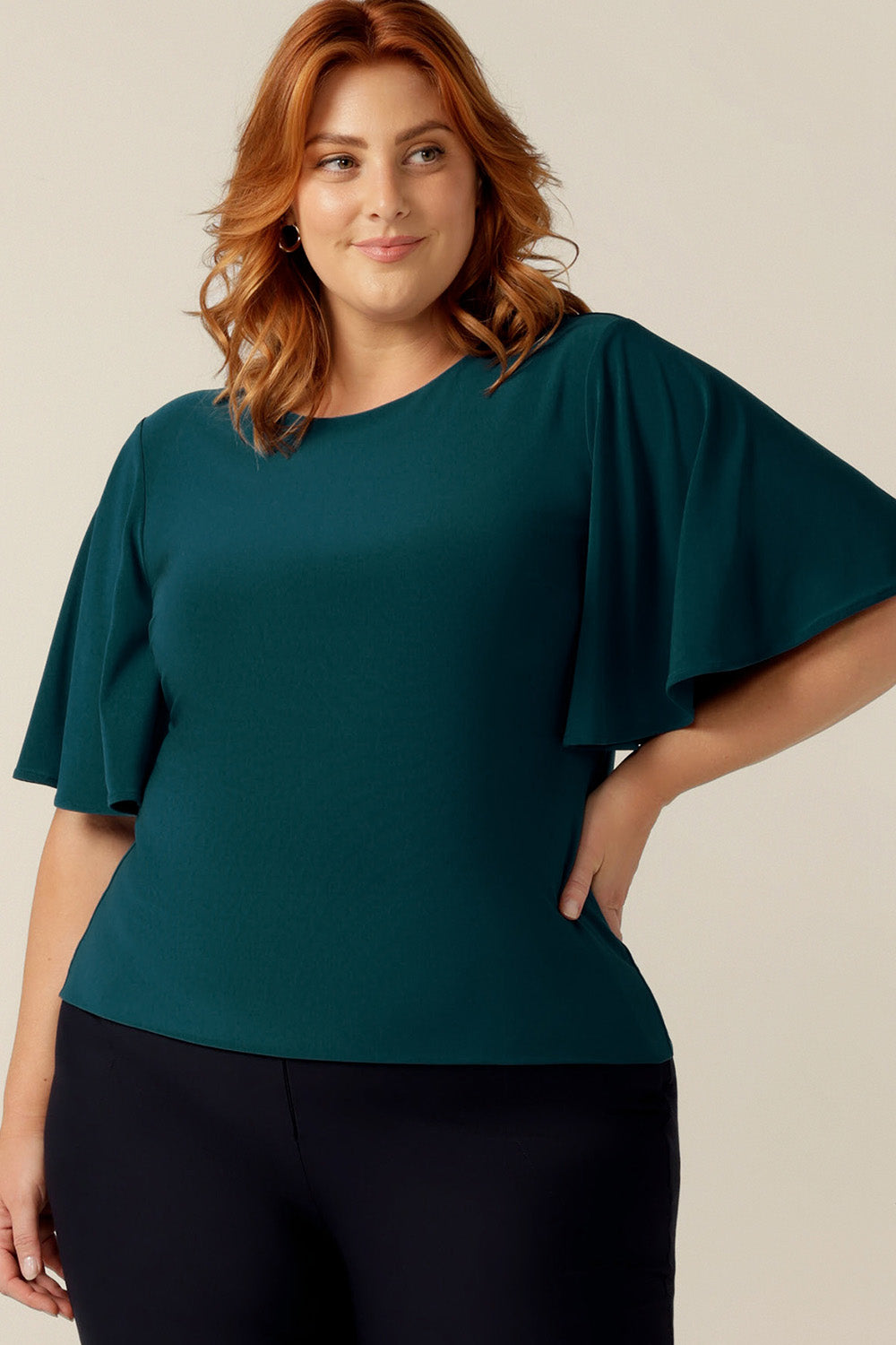 plus size woman wearing a fitted jersey top for work wear and corporate dressing. The top features a high round neckline and flutter sleeves. The top is made-in-Australia by women's clothing brand, Leina and Fleur, for petite to curvy women.