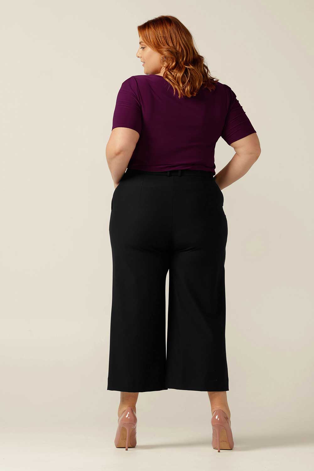 Size 18 curvy woman wearing tailored wide leg, cropped-length, black work trousers. The black pants are worn with a boat-neck short sleeve jersey top, both made in Australia, for a complete work wear look.