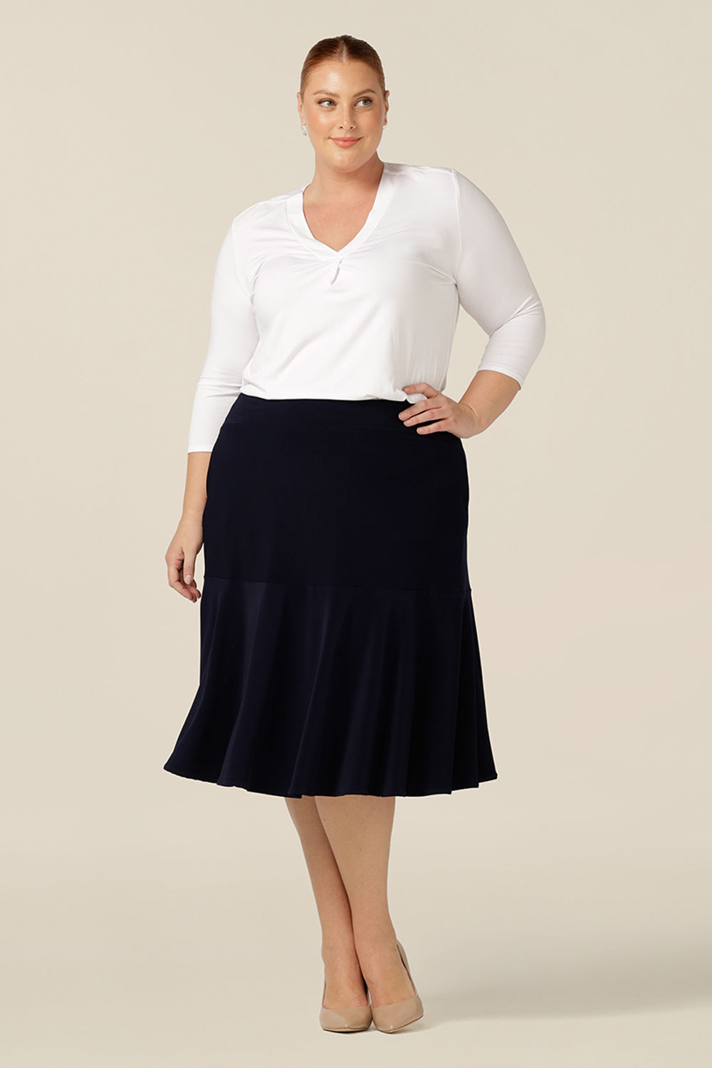 a size 18, fuller figure woman wears a knee-length, navy blue jersey skirt with ruffle hem. The skirt is worn with a white, long sleeve, bamboo jersey top for a smart-casual look that translates for easy work wear style.