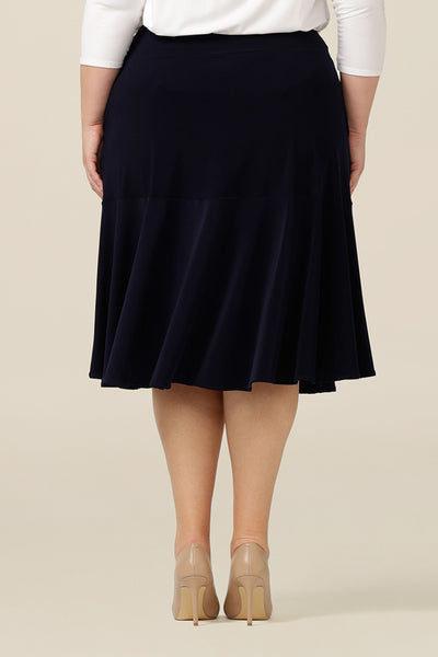 Back view of a navy blue, below-the-knee-length skirt with ruffle hemline worn by a plus size, size 18 woman. A pull-on skirt in stretch jersey fabric, this is a comfortable skirt for all-day work wear.