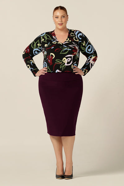 A knee length, pull-on tube skirt in Mulberry stretch jersey is worn with an abstract printed V-neck top with long sleeves all by Australia and New Zealand womens clothing brand, L&F.