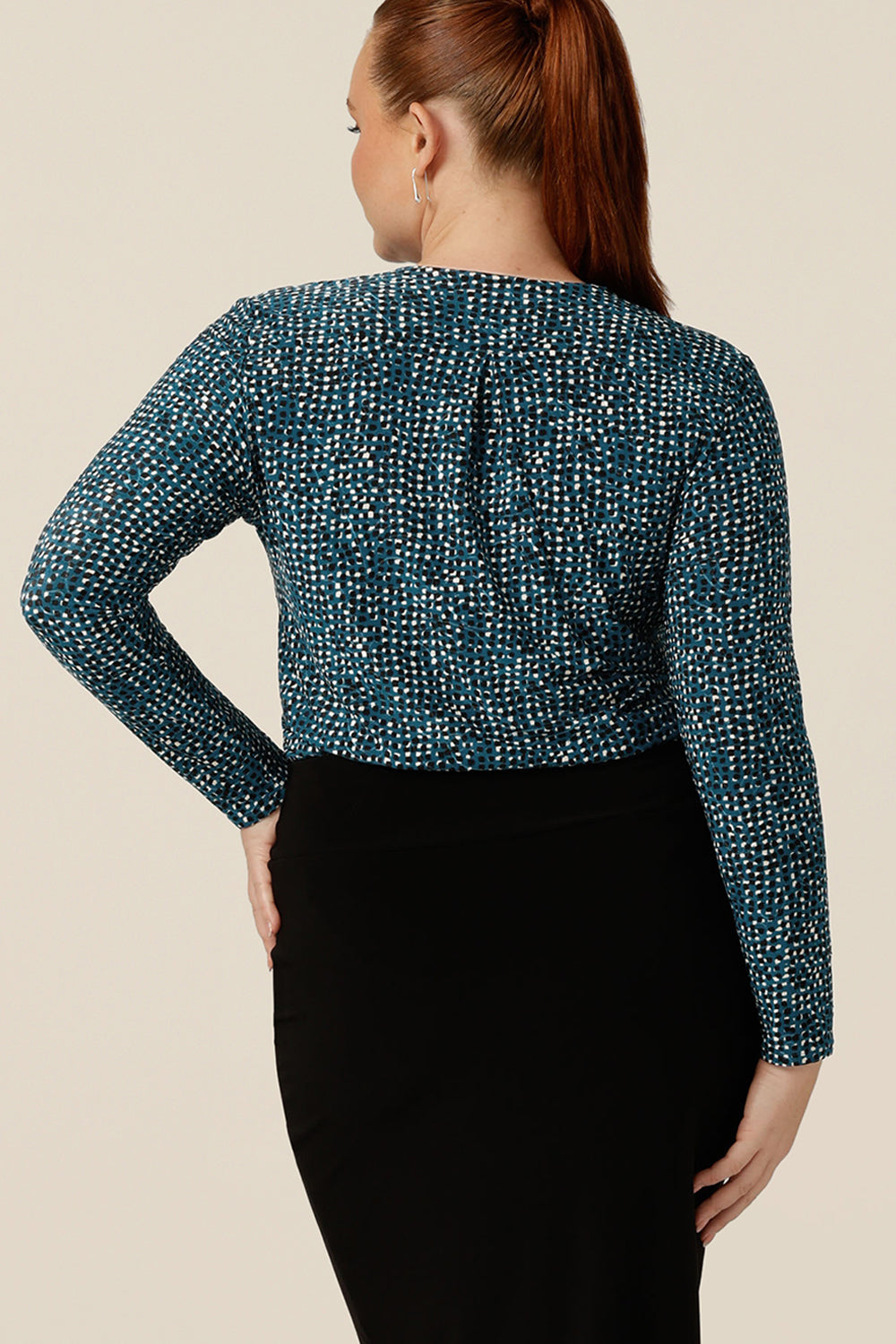 A size 12 curvy woman wears a long sleeve, V-neck jersey top in blue, black and white printed jersey jacquard. Tucked in to a black tube skirt, this jersey top works for corporate office wear. Available in an inclusive size range of 8-24.