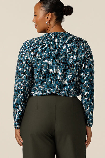 A size 18, fuller figure woman wears a long sleeve, V-neck jersey top in blue, black and white printed jersey jacquard. Tucked in to olive green tailored work pants, this long sleeve top for women works for work and casual wear. Made for petite to plus size women, shop this workwear top in sizes 8-24.