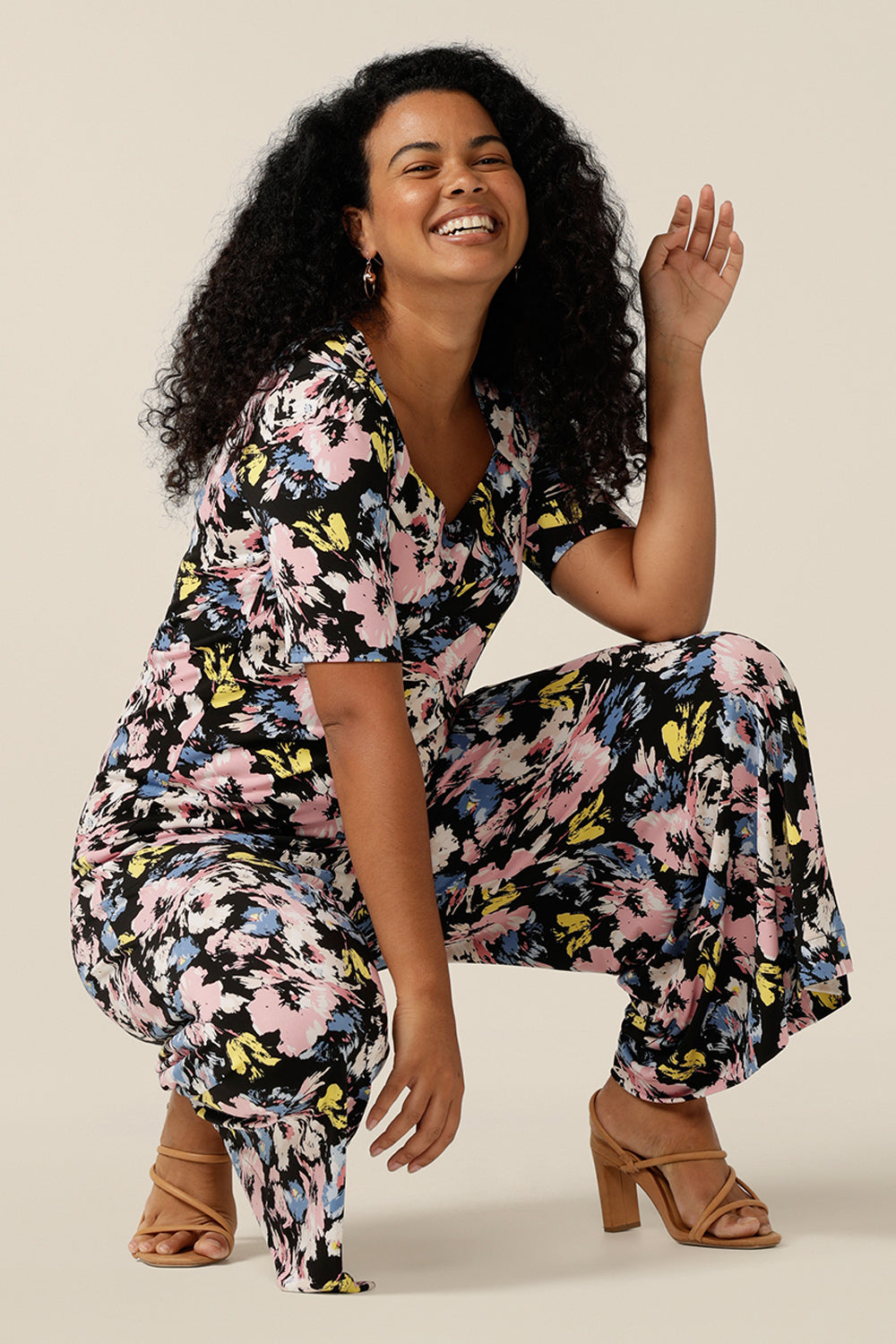 A sizes 12 woman wears a short-sleeve printed jersey top with matching wide-leg printed pants to create a faux jumpsuit look. The top has a squared scoop neckline and supported bust. The trousers are a pull-on jersey pant cropped in length. Both the women's top and pants feature a floral print with a black base and pastel flowers. Both are available to shop online from sizes 8 to size 16 and plus sizes 18 to size 24 at Leina and Fleur. 