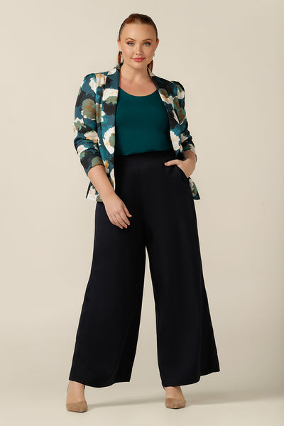 a size 12, curvy woman wears a round neck, long sleeve, fitted top in green bamboo jersey. In natural fibres, the bamboo jersey top is worn with wide leg, navy blue pants and a soft tailoring blazer jacket - both women's top, trousers and blazer are lightweight, breathable and made in Australia for smart casual workwear.