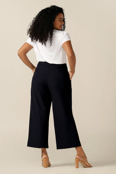 A size 12 curvy woman wears wide-leg, cropped length pants in Navy. Worn with a white top in bamboo jersey, the pants are styled as modern work wear trousers. With front pleats, side pockets and in stretch jersey, they are cut as a comfortable fit pant for all-day corporate wear.