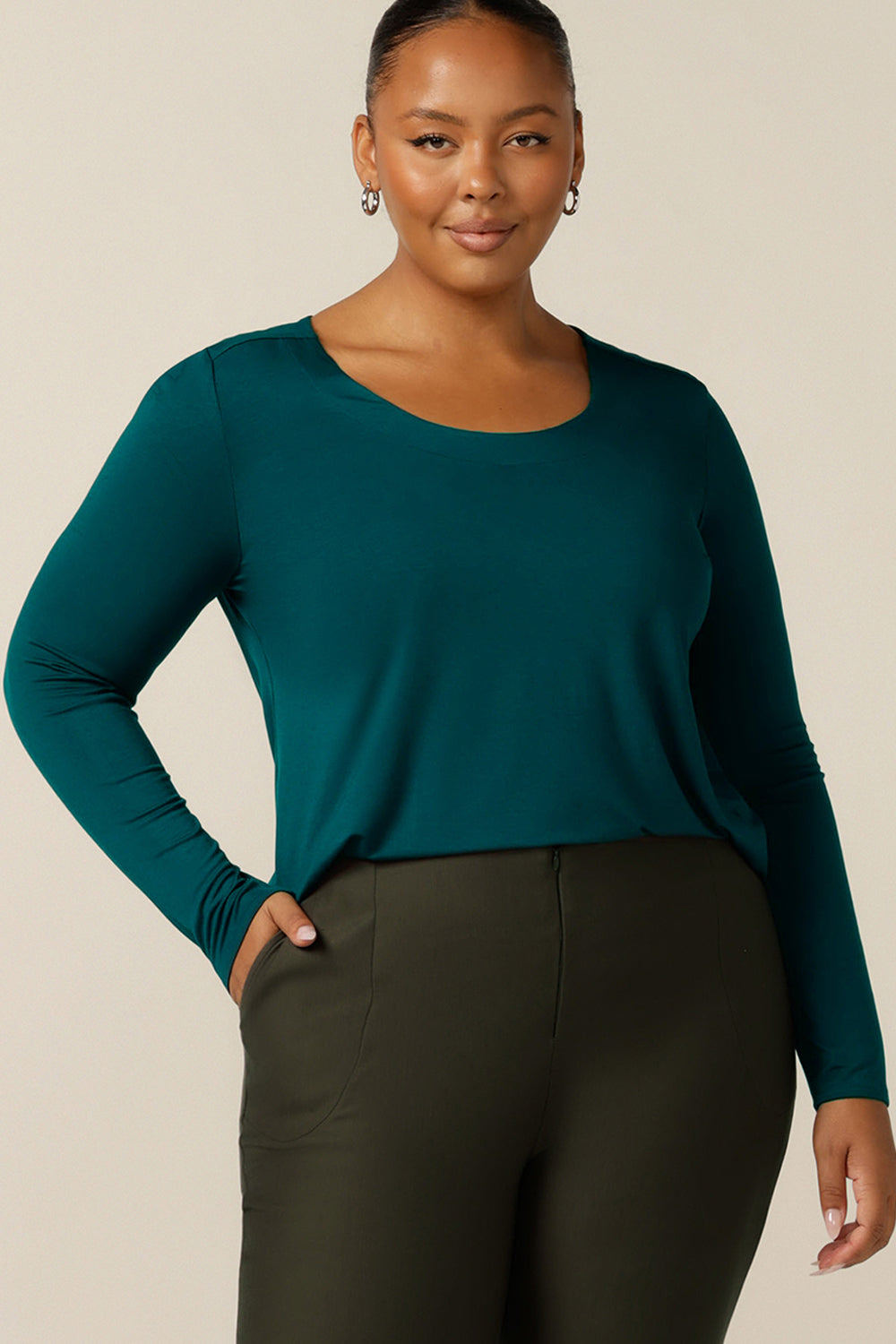 a size 18, fuller figure woman wears a round neck, long sleeve, fitted top in green bamboo jersey. In natural fibres, the bamboo jersey top is lightweight, breathable and comfortable for casual or work wear.