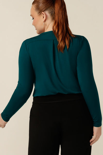 back view of a size 12, curvy woman wears a round neck, long sleeve, fitted top in green bamboo jersey. Made in Australia, this natural fibre top is available to shop online in an inclusive size range of 8-24.