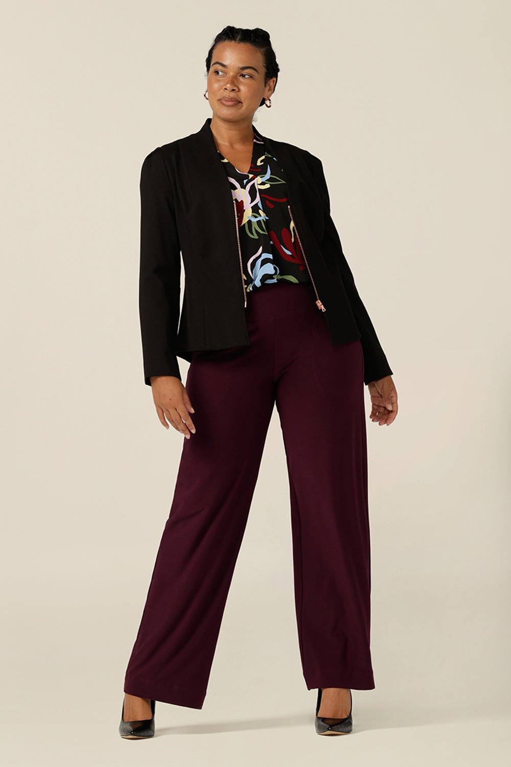 a size 12 curvy woman wears a wide-leg, pull-on pant in Mulberry red jersey. A full-length, straight-leg trouser with wide legs, these stretch pants is worn with a black corporate jacket and long sleeve jersey top for a work wear look. 