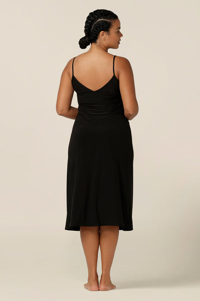 back view of a size 12 woman wearing a midi-length, reversible slip in black, slinky jersey fabric. The slip has thin straps and is worn with a scoop neck to the front, and V back..