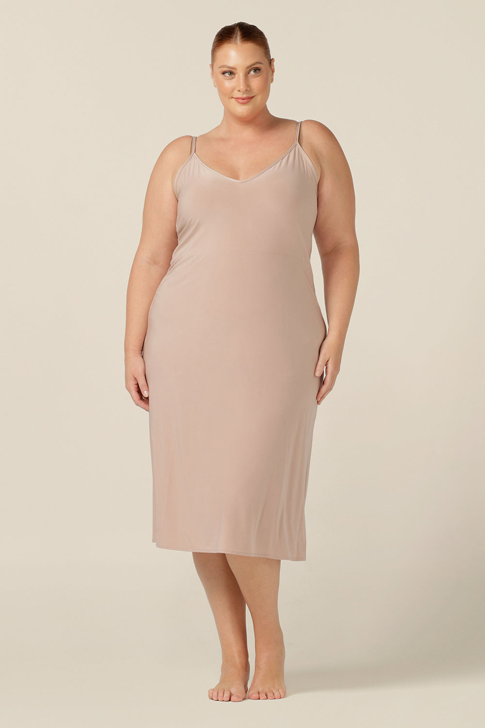 A fuller figure woman wears a midi-length, reversible slip in nude slinky stretch jersey. Worn with a V neck to the front, this slip can flip to show a scoop neck. With a skirt length finishing below the knee, this neutral midi slip gives a smooth layer under dresses and skirts.
