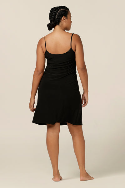 Back view of a size 12 woman wearing a above-the-knee length reversible slip in black, slinky jersey fabric. The slip has thin straps and is worn with a V neck to the front, scoop neck to the back. Made in Australia by women's clothing brand, L&F lounge wear