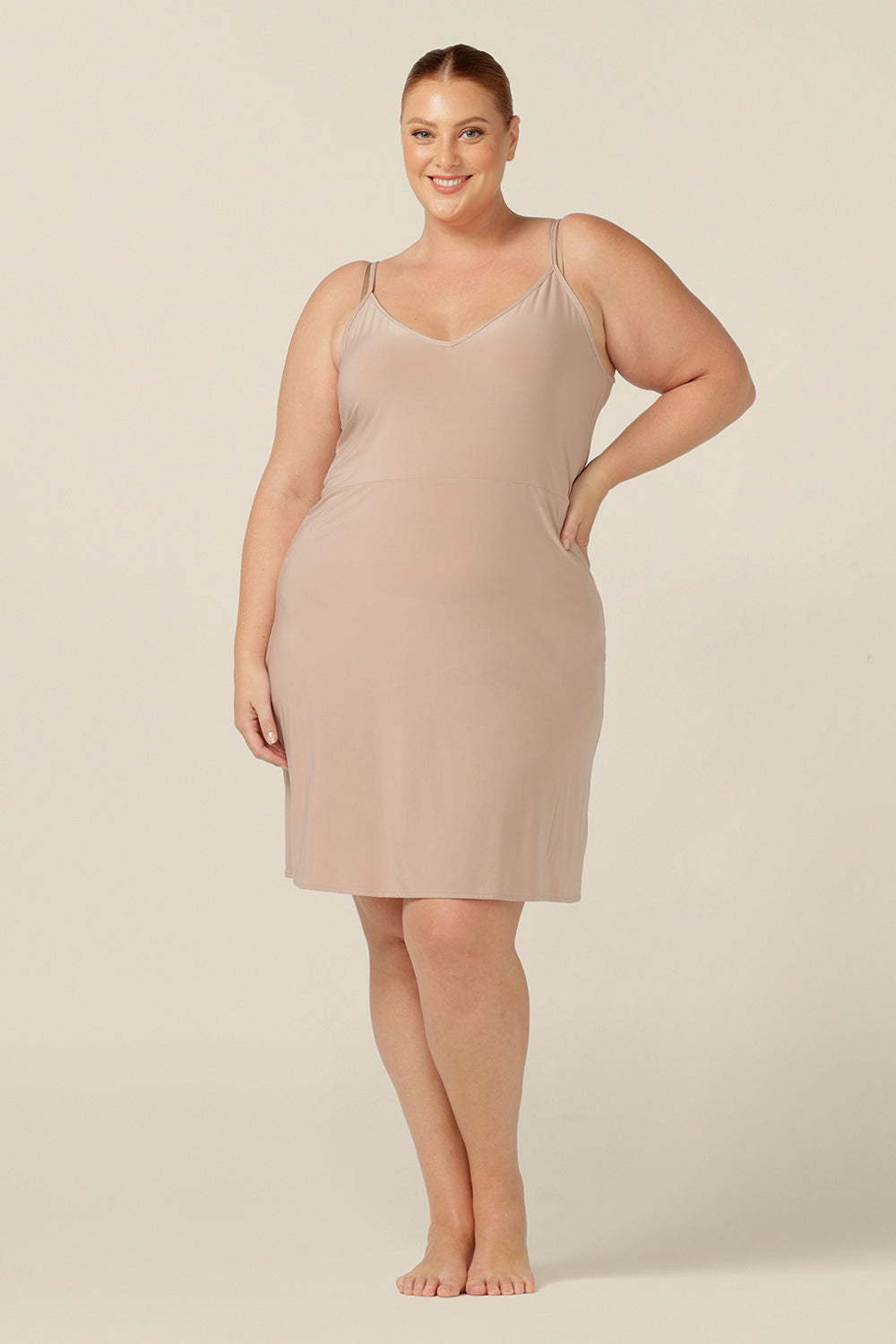 plus size, size 18 woman wears a nude, mini-length slip. A reversible slip, this flesh coloured under garment can have a V-neck or a scoop neck to give a smooth layer under dresses and skirts. Great for wearing around the house as loungewear - Australian womens fashion