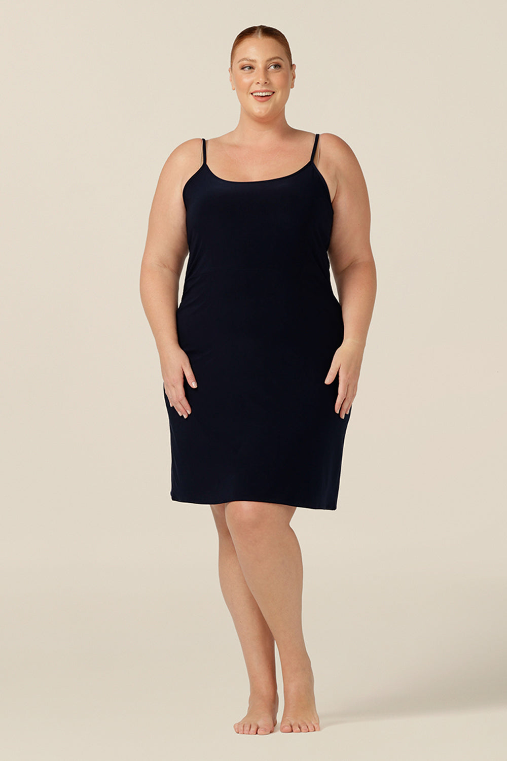 plus size slip dress for lounge wear - size 18 woman wears a navy, mini-length slip, shown with a scoop neckline and thin straps.. A reversible slip, this under garment can have a V-neck or a scoop neck to give a smooth layer under dresses and skirts.