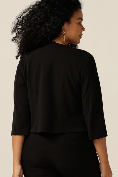 A size 12 woman wears a soft tailoring work wear jacket in black jersey. An open-front, collarless jacket with 3/4 sleeves, this jacket works well with work tops and pants. 