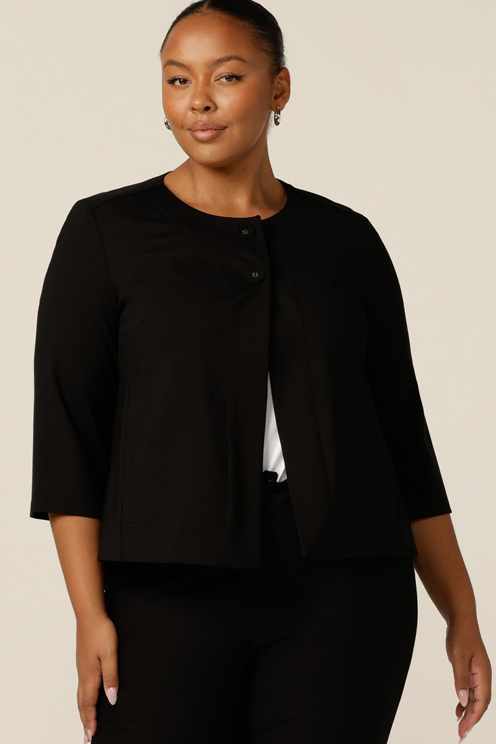 A plus size, size 18 woman wears a black swing jacket for alternative corporate wear. Featuring round collarless neckline with 2-button fastenings, 3/4 sleeves and swing back, this black jacket has a sophisticated corporate elegance with made-in-Australia quality.