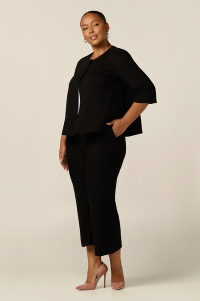 A plus size, size 18 woman wears a black swing jacket for alternative corporate wear. Featuring round collarless neckline with 2-button fastenings, 3/4 sleeves and swing back, this black jacket has a sophisticated corporate elegance with made-in-Australia quality. Worn with black cropped leg pants, this is a work wear look that empowers fuller figures.
