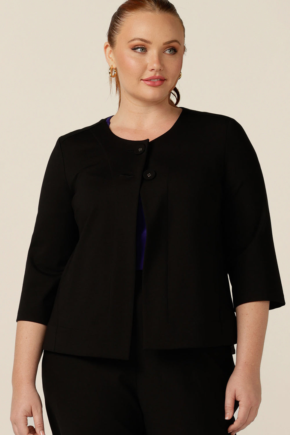 A size 12 woman wears a round neck, collarless jacket with 3/4 sleeves. In black ponte jersey, this comfortable jacket comes in an inclusive size range for petite to plus size women.