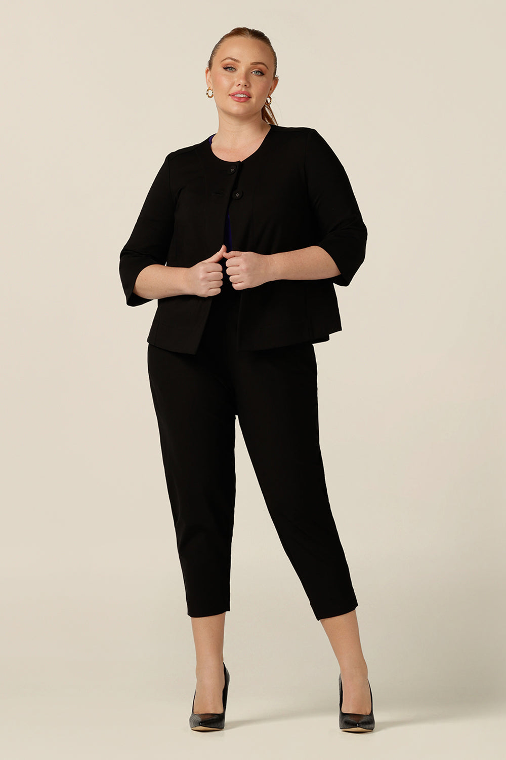 A curvy size 12 woman wears a black swing jacket for alternative workwear. Featuring round collarless neckline with 2-button fastenings, 3/4 sleeves and swing back, this black jacket has a sophisticated corporate elegance with made-in-Australia quality.