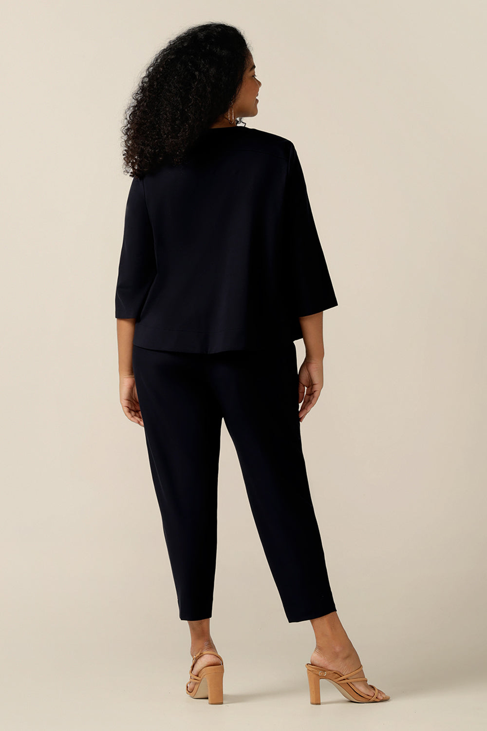 A curvy size 12 woman wears a round neck navy work wear jacket with 3/4 sleeves and a swing back.